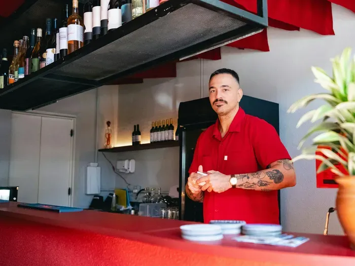 Small bar owner in red shirt behind counter with bottles, illustrating trusted local pros on Local Service Check